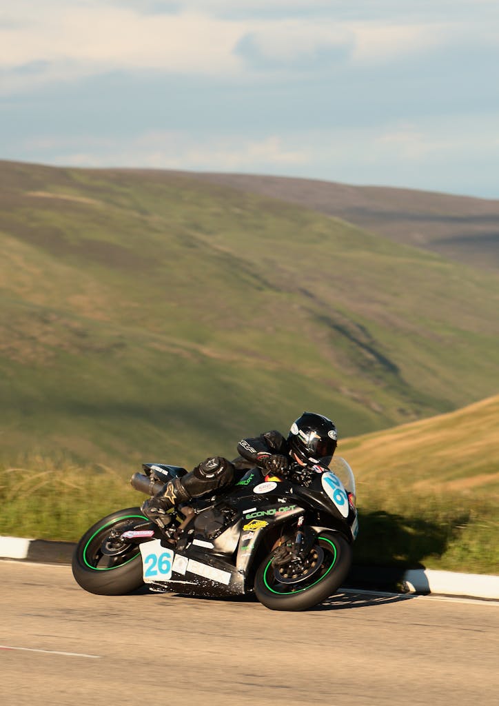 Motorcycle rider speeding through scenic Isle of Man during a race event on a winding road.